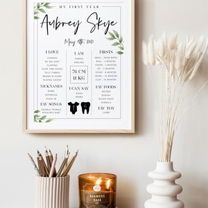May include: A printable baby milestone chart with a white background and green foliage accents. The chart is titled "My First Year" and features the name "Aubrey Skye" with the date "May 18th, 2021". The chart includes sections for "I Love", "I Am", "Firsts", "Nicknames", "I Can Say", "Fav Songs", "Fav Foods", and "Fav Toy".