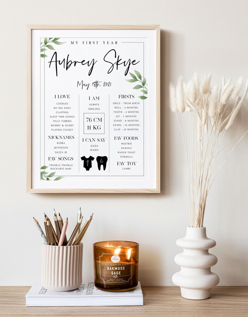 May include: A printable baby milestone chart with a white background and green foliage accents. The chart is titled "My First Year" and features the name "Aubrey Skye" with the date "May 18th, 2021". The chart includes sections for "I Love", "I Am", "Firsts", "Nicknames", "I Can Say", "Fav Songs", "Fav Foods", and "Fav Toy".