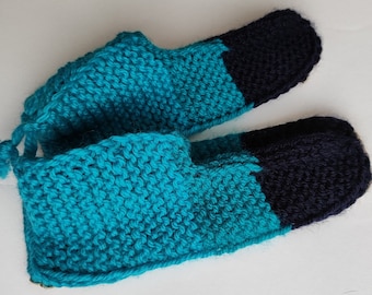May include: A pair of teal blue knitted slippers with black toe tips. The slippers are made with a soft, cozy yarn and have a simple, comfortable design.