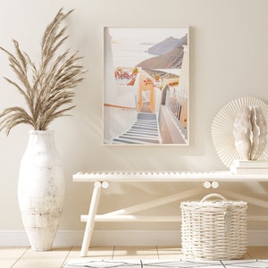 May include: A whitewashed building with a stairway leading up to an archway. The building is situated on a cliff overlooking the ocean. The image is framed in a white frame.