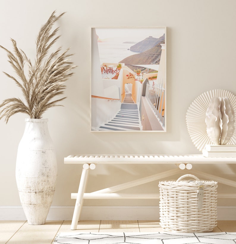 May include: A whitewashed building with a stairway leading up to an archway. The building is situated on a cliff overlooking the ocean. The image is framed in a white frame.