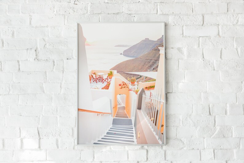 May include: A white building with a staircase leading up to a patio with a view of the ocean and a hillside. The patio has a table and chairs.