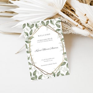 May include: A white card with a gold geometric frame and green leaves around the border. The text on the card reads "Welcome to the Quinceañera Misa de Kiara Maria Alvarez el 12 de Noviembre 2022 Incarnation Catholic Church".