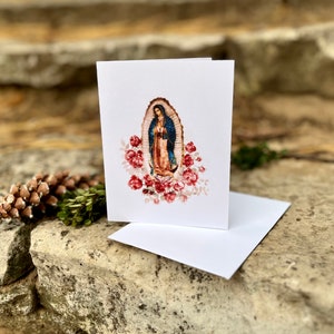 Op de afbeelding: Een witte kaart met een kleurrijk beeld van de Maagd Maria, omringd door rode rozen. Het beeld is in een ovale lijst.