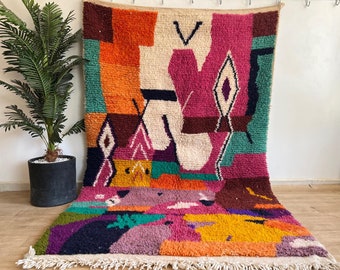 Può includere: Un tappeto astratto colorato con forme geometriche in tonalità di rosa, arancio, verde e marrone. Il tappeto ha un bordo a frange ed è fatto di lana.