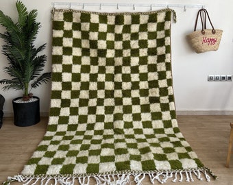 May include: A green and white checkered rug with fringe. The rug is hanging on a wall with a straw hat above it.