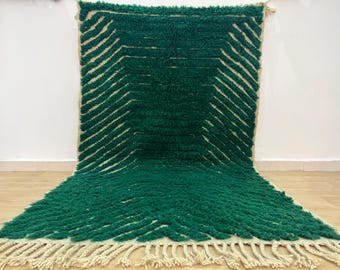 May include: A green and cream handwoven rug with a geometric pattern. The rug has a fringe border.