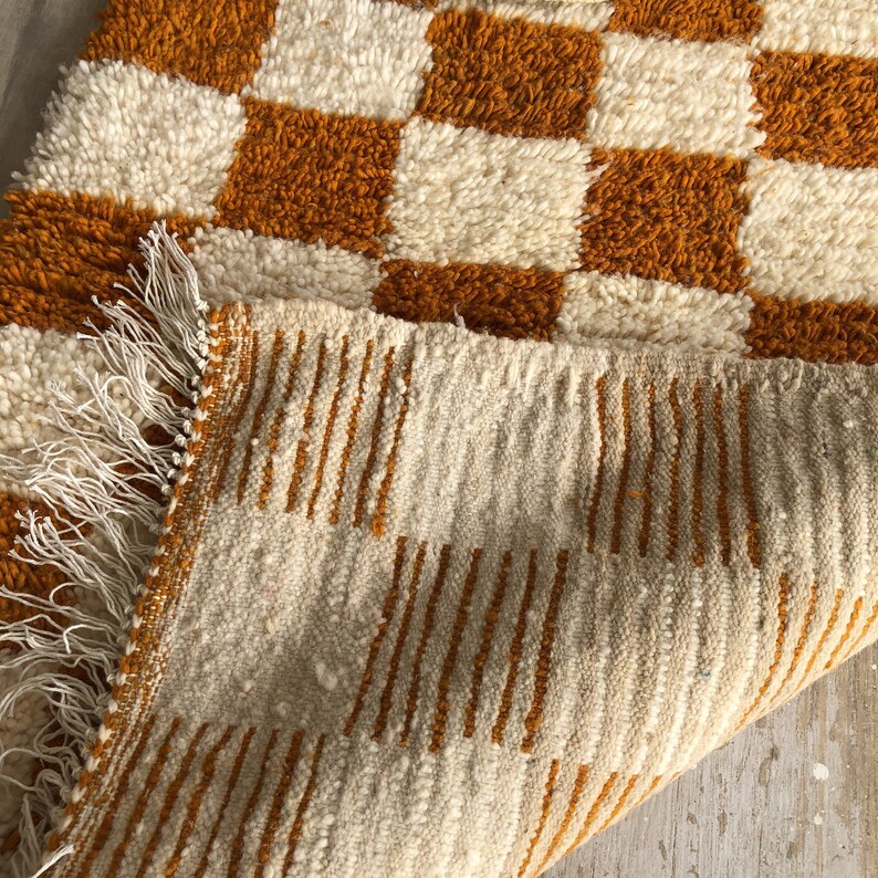 May include: A white and orange checkered rug with a fringe border. The rug is made of a soft, fluffy material.