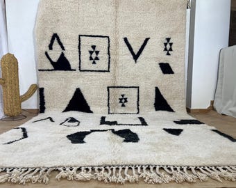 May include: A white and black Moroccan rug with geometric patterns. The rug has a fringe border and is made of wool.