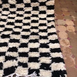 May include: Black and white checkered rug with a fringe border. The rug is made of a thick, fluffy material.