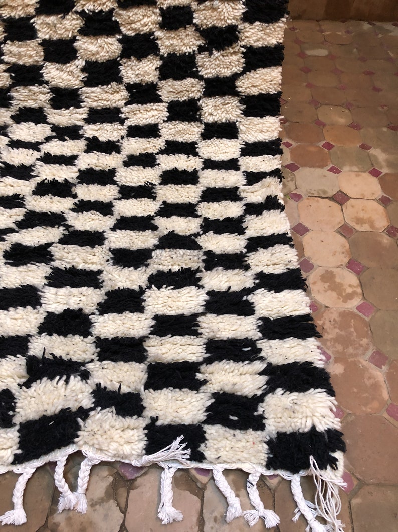 May include: Black and white checkered rug with a fringe border. The rug is made of a thick, fluffy material.