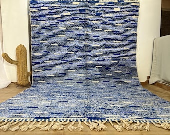 Puede incluir: Una alfombra de rayas azules y blancas con un borde de flecos. La alfombra está hecha de lana y tiene una textura suave y esponjosa.