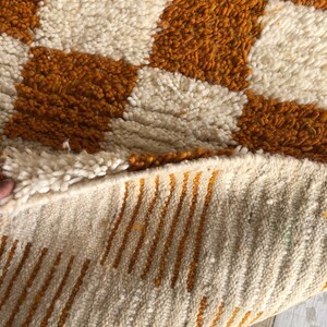 May include: Close-up of a white and orange woven rug with a geometric pattern. The rug is folded in half, showing the underside with a striped pattern.