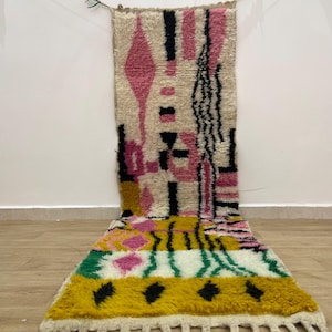 Peut inclure: Un tapis long et rectangulaire avec un motif abstrait coloré. Le tapis présente des formes géométriques dans des tons de rose, jaune, vert, noir et blanc. Le tapis a une frange sur le bord inférieur.