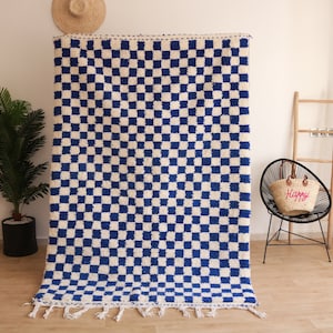 Puede incluir: Una alfombra a cuadros azules y blancos con flecos. La alfombra está hecha de un material suave y esponjoso y tiene un patrón geométrico.