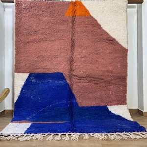 May include: A geometric patterned rug with a white, pink, blue, and orange color scheme. The rug has a fringe border.