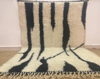 May include: A white and black Moroccan rug with a geometric pattern. The rug has a fringe border and is made of wool.