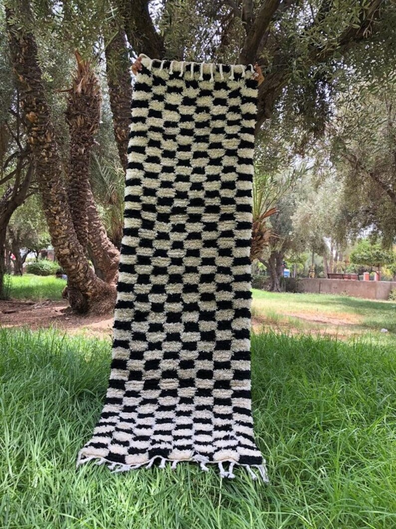 May include: Black and white checkered rug with a fringe border. The rug is made of a soft, fluffy material and is hanging from a tree branch.