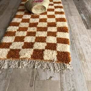 May include: A brown and white checkered rug with a fringe border. The rug is made of a soft, fluffy material.