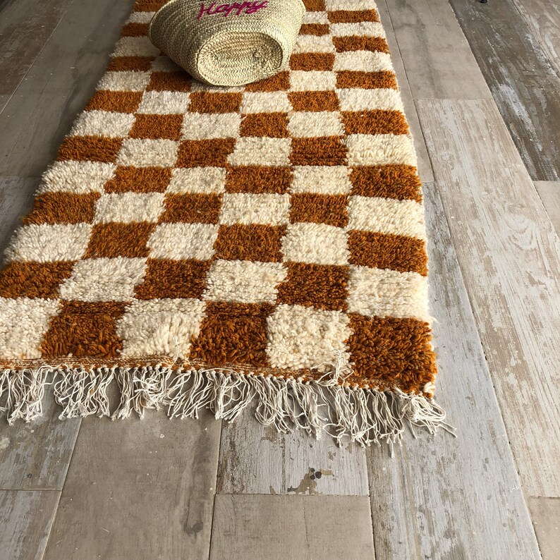 May include: A brown and white checkered rug with a fringe border. The rug is made of a soft, fluffy material.