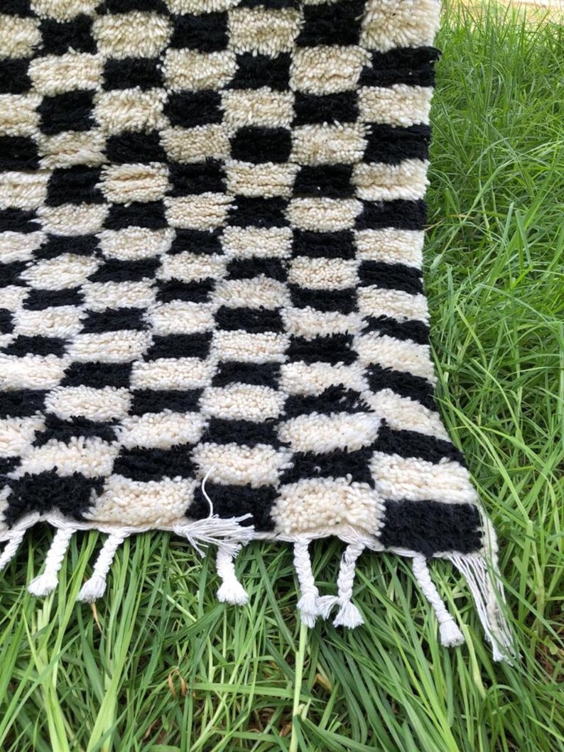 May include: Black and white checkered rug with a fringe border. The rug is made of a soft, fluffy material and has a geometric pattern.