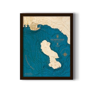 May include: A wooden map of Dubrovnik, Croatia, with a blue and brown color scheme. The map shows the coastline and surrounding waters. The text "Dubrovnik" is printed in gold at the top of the map.