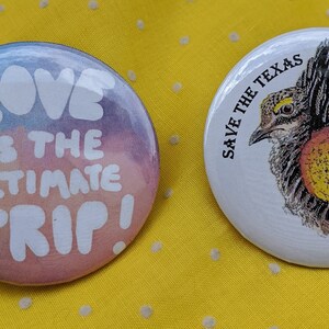 K&ouml;nnte beinhalten: Zwei runde Buttons auf gelbem Hintergrund. Ein Button hat ein Aquarelldesign mit dem Text "LOVE IS THE ULTIMATE TRIP!". Der andere Button sagt "SAVE THE TEXAS PRAIRIE CHICKEN" und zeigt eine Vogelillustration.