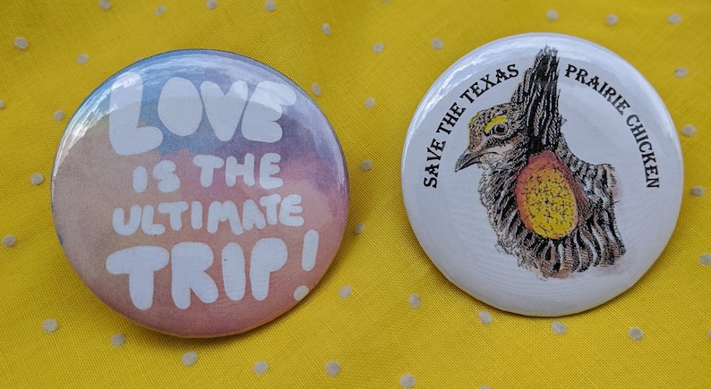 K&ouml;nnte beinhalten: Zwei runde Buttons auf gelbem Hintergrund. Ein Button hat ein Aquarelldesign mit dem Text "LOVE IS THE ULTIMATE TRIP!". Der andere Button sagt "SAVE THE TEXAS PRAIRIE CHICKEN" und zeigt eine Vogelillustration.