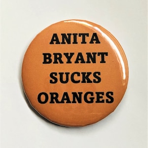 以下が含まれることがあります： 「ANITA BRYANT SUCKS ORANGES」と黒い文字が書かれたオレンジ色の丸いボタン。ボタンは光沢のある仕上がりです。テキストは中央に配置され、太字のサンセリフ体です。