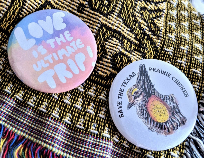K&ouml;nnte beinhalten: Zwei runde Ansteckbuttons. Einer zeigt den Text "LOVE IS THE ULTIMATE TRIP!" in Wei&szlig; auf pastellfarbenem Hintergrund. Der andere Button zeigt eine detaillierte Illustration eines Pr&auml;riehuhns mit dem Text "SAVE THE TEXAS PRAIRIE CHICKEN".