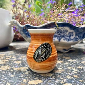 May include: A small, brown and white ceramic vase with a black and white design. The vase has a rounded bottom and a narrow neck.