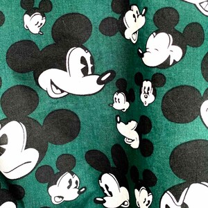 May include: A green fabric with a repeating pattern of black and white Mickey Mouse heads.
