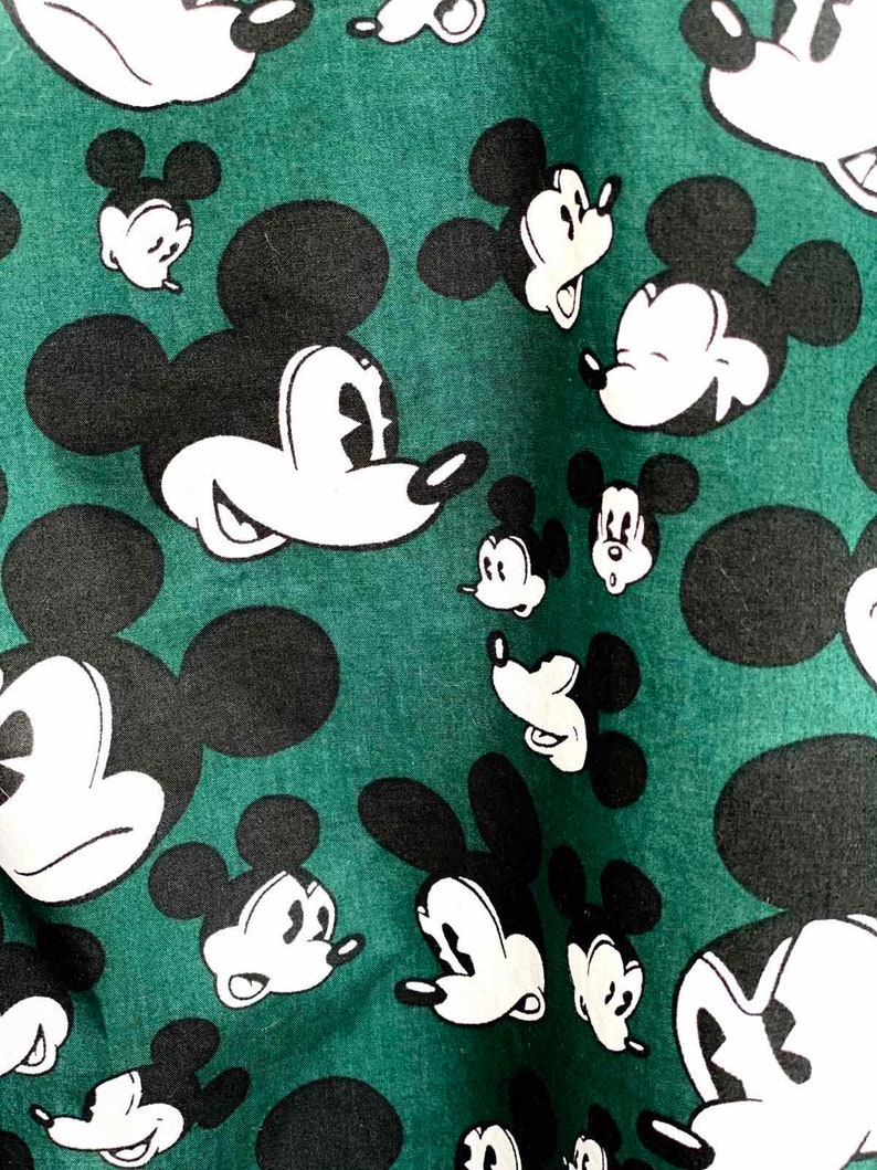 May include: A green fabric with a repeating pattern of black and white Mickey Mouse heads.