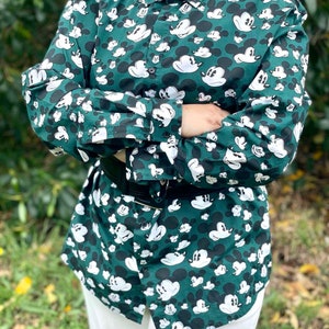 May include: A green long-sleeved button-down shirt with a white Mickey Mouse print all over.