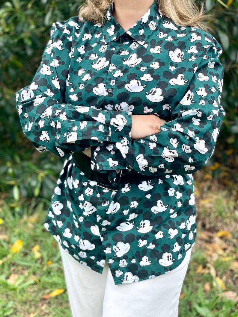 May include: A green long-sleeved button-down shirt with a white Mickey Mouse print all over.