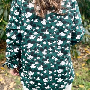 May include: A green long-sleeved button-down shirt with a white Mickey Mouse print all over.