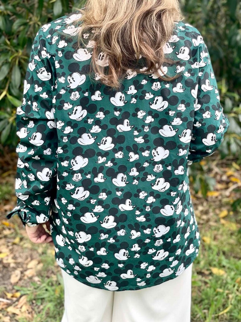 May include: A green long-sleeved button-down shirt with a white Mickey Mouse print all over.