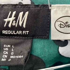 May include: A black and white tag with the text "H&M REGULAR FIT" and size information. A white tag with the text "Disney" is attached to the right.
