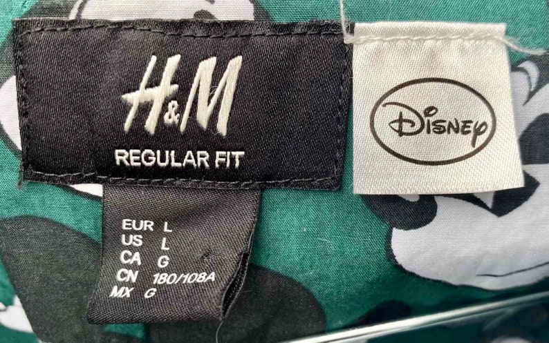 May include: A black and white tag with the text "H&M REGULAR FIT" and size information. A white tag with the text "Disney" is attached to the right.