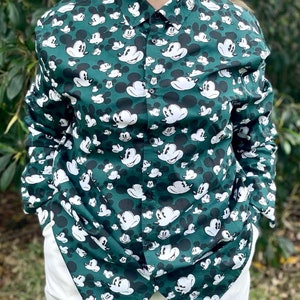 May include: A green long-sleeved button-down shirt with a white Mickey Mouse print all over.
