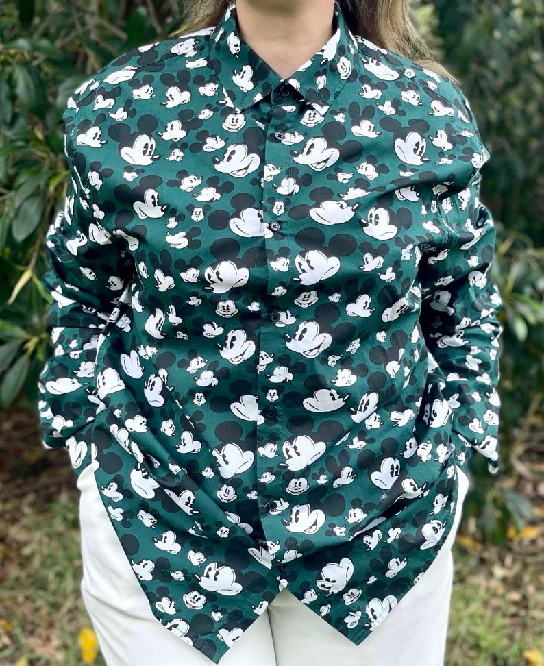 May include: A green long-sleeved button-down shirt with a white Mickey Mouse print all over.