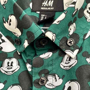 May include: A green button-down shirt with a Mickey Mouse print. The shirt has a label that says "H&M REGULAR FIT" and "EUR L US L CA L".