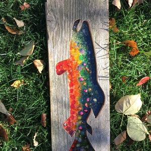 May include: A rainbow-colored fish made of glass mosaic tiles is set into a reclaimed wood panel. The fish is outlined in black and has a realistic shape.