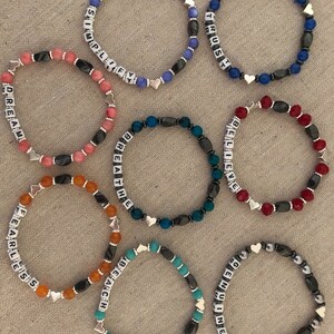 May include: Eight bracelets with black and silver beads and white letter beads spelling out the words "DREAM", "SIMPLIFY", "TRUST", "BELIEVE", "BREATHE", "FEARLESS", "REACH", and "GENUINE".
