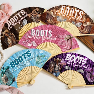May include: Five folding hand fans with wooden ribs, each featuring the text "BOOTS On the Ground" and western-themed graphics including cowboy boots, hats, horses, and diamonds in brown, pink, blue, and purple glitter and wood-grain patterns.