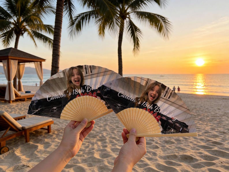 May include: Two open hand fans with a photo of a person and the text "Caitlin's 18th Birthday". The fans have a natural wood handle and a printed image. The background shows a beach scene with palm trees and a sunset.