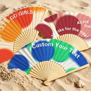 May include: Three folding hand fans with wooden ribs and fabric leaves. One fan is orange with the text LET'S GO GIRLS!, one is red with the text All my love, thanks for the ride!, and one is blue and green with the text Custom Your Text.
