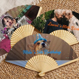 May include: A collection of personalized hand fans with images and text. One fan features a young person with the text "Iris's 20th Birthday." Another fan displays two older adults with the text "Laurel's 80th Birthday." A third fan shows a dog with the text "Milo's 5th Birthday."