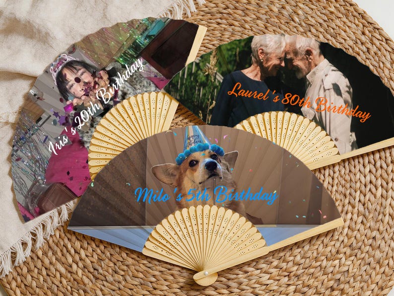 May include: A collection of personalized hand fans with images and text. One fan features a young person with the text "Iris's 20th Birthday." Another fan displays two older adults with the text "Laurel's 80th Birthday." A third fan shows a dog with the text "Milo's 5th Birthday."