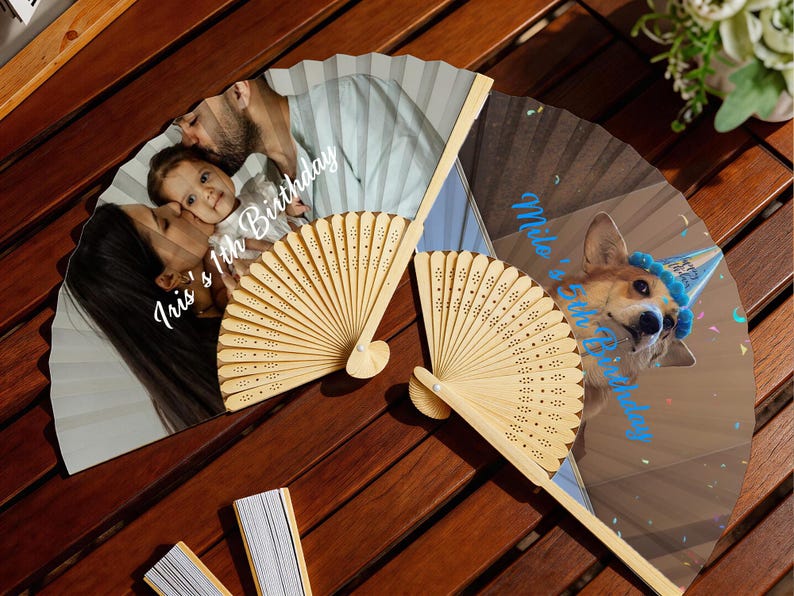 May include: Two personalized hand fans with wooden handles. One fan features a family photo with the text "Iris's 1th Birthday". The other fan displays a dog wearing a party hat with the text "Milo's 1th Birthday".